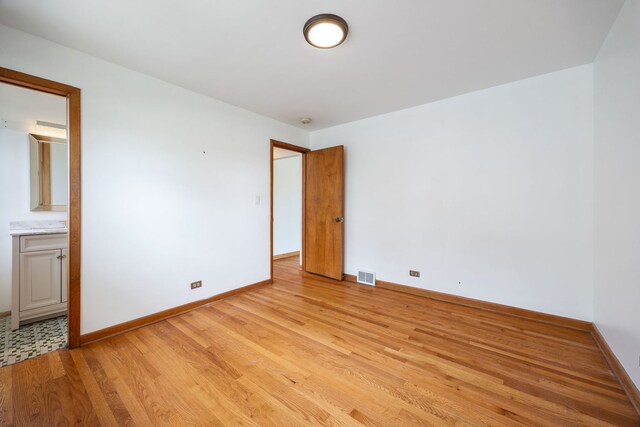 unfurnished bedroom featuring light wood-style floors, baseboards, and ensuite bath