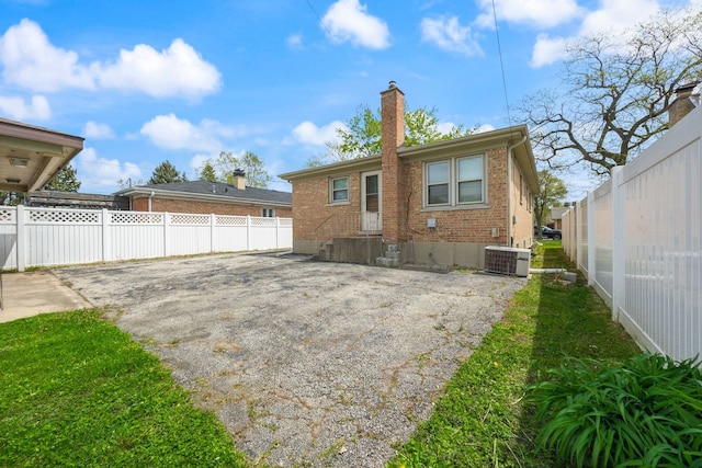 rear view of house featuring brick siding, a chimney, fence, and driveway