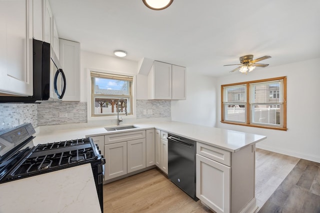 kitchen featuring black appliances, a sink, a peninsula, and light wood finished floors