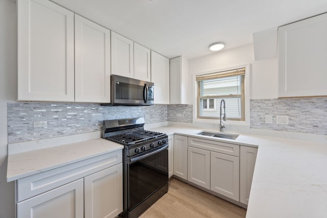 kitchen featuring stainless steel microwave, range with gas stovetop, a sink, light stone counters, and white cabinets