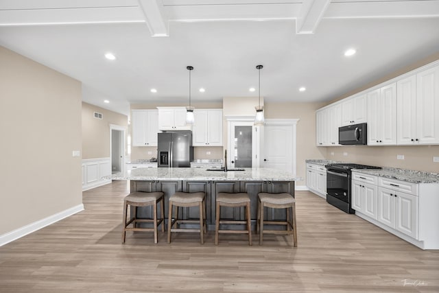 kitchen with black appliances, a sink, light wood-style floors, white cabinets, and a wainscoted wall
