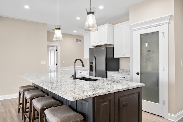 kitchen with stainless steel fridge, a sink, white cabinetry, light wood-type flooring, and an island with sink
