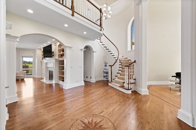 6590 Beech Ln, Libertyville, IL 60048 - entrance foyer featuring decorative columns, light wood-style flooring, a fireplace with flush hearth, arched walkways, and a high ceiling