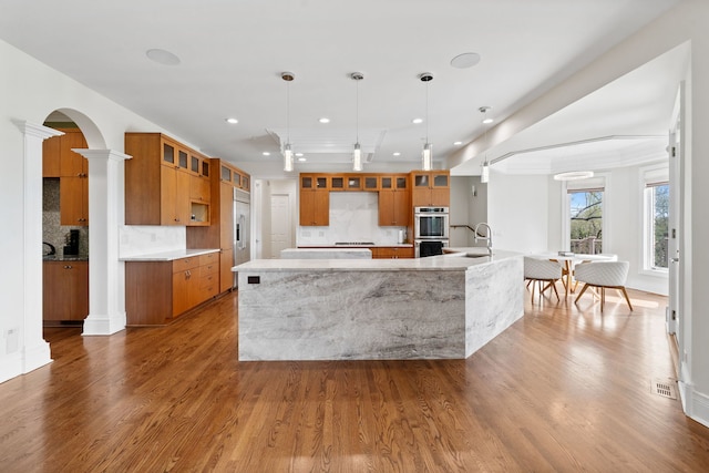 6590 Beech Ln, Libertyville, IL 60048 - kitchen with appliances with stainless steel finishes, brown cabinets, a sink, a large island, and decorative columns