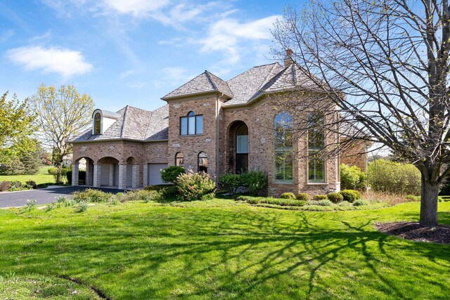6590 Beech Ln, Libertyville, IL 60048 - french country inspired facade featuring driveway, brick siding, a front lawn, a chimney, and a high end roof