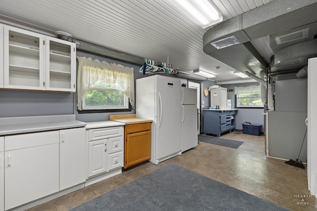 kitchen featuring freestanding refrigerator, light countertops, glass insert cabinets, and finished concrete flooring