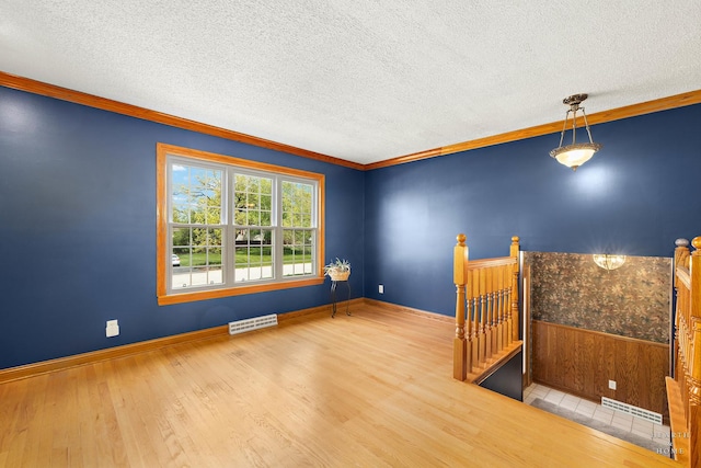 empty room with wood finished floors, ornamental molding, a textured ceiling, wainscoting, and baseboards