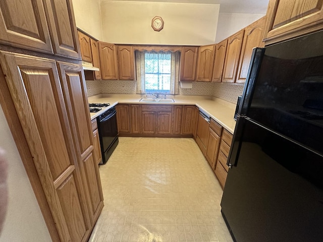 kitchen with freestanding refrigerator, range with gas stovetop, a sink, under cabinet range hood, and brown cabinets
