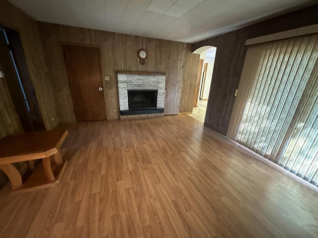 unfurnished living room featuring wooden walls, arched walkways, light wood finished floors, and a fireplace with raised hearth
