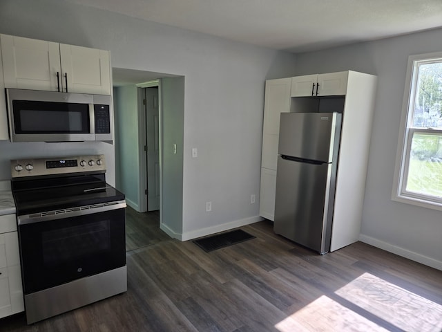kitchen with appliances with stainless steel finishes, white cabinets, baseboards, and dark wood-style flooring