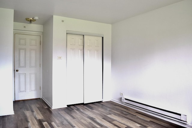 unfurnished bedroom featuring baseboard heating, dark wood-style floors, a closet, and baseboards