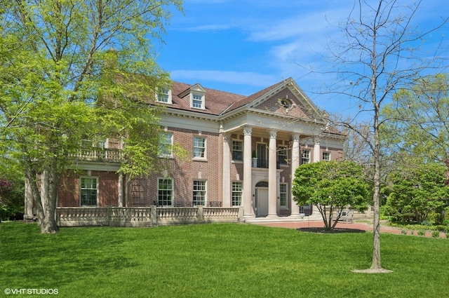 greek revival house featuring a balcony, brick siding, and a front lawn