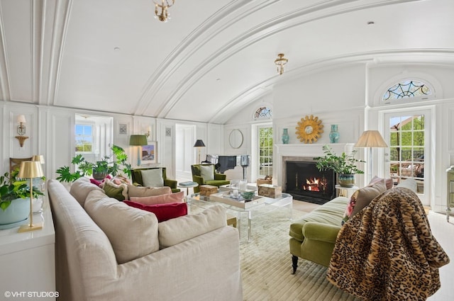 living area with a lit fireplace, plenty of natural light, vaulted ceiling, and a decorative wall