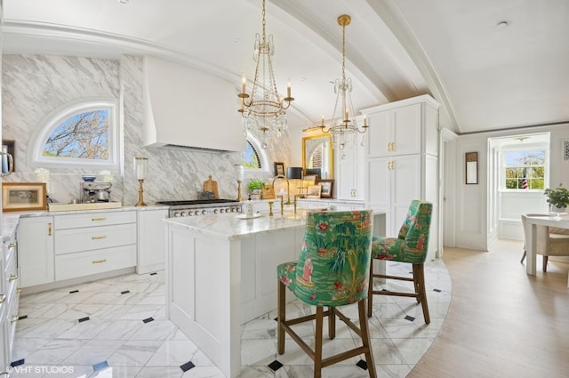 kitchen featuring ornamental molding, light stone countertops, a chandelier, white cabinets, and an island with sink