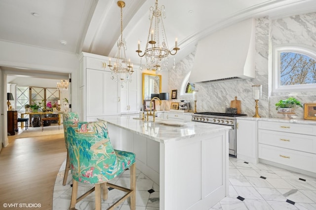 kitchen featuring stainless steel stove, a chandelier, custom exhaust hood, light stone countertops, and white cabinets