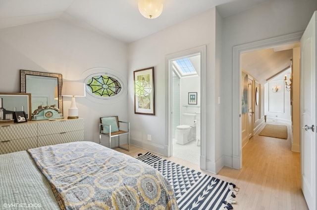 bedroom with vaulted ceiling, light wood finished floors, baseboards, and ensuite bathroom