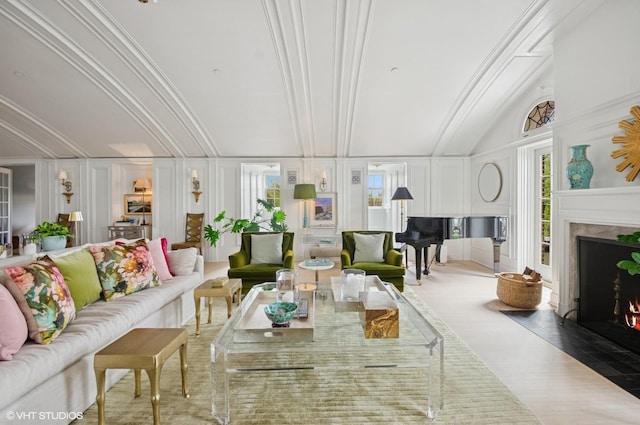 living area with a decorative wall, a high end fireplace, healthy amount of natural light, wood finished floors, and lofted ceiling