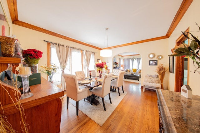 dining area featuring arched walkways, light wood finished floors, and crown molding