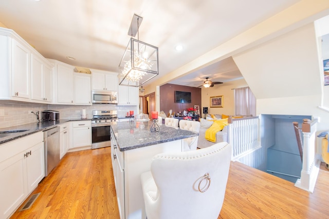 kitchen featuring stainless steel appliances, a kitchen island, light wood finished floors, open floor plan, and dark stone countertops