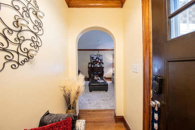 corridor featuring arched walkways, crown molding, wood finished floors, and baseboards