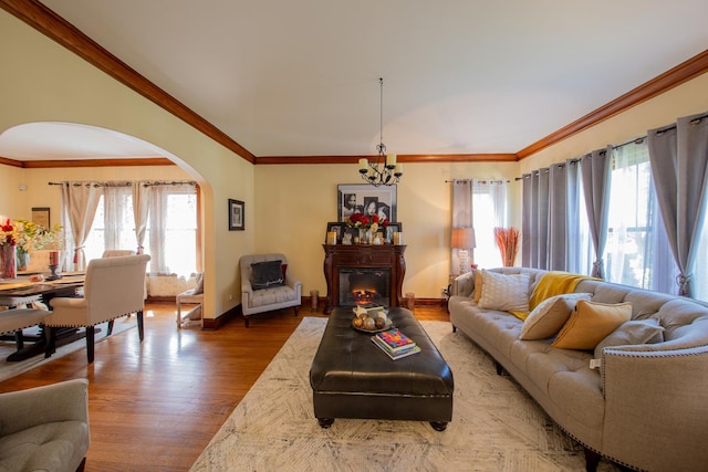 living area featuring arched walkways, wood finished floors, a chandelier, baseboards, and crown molding