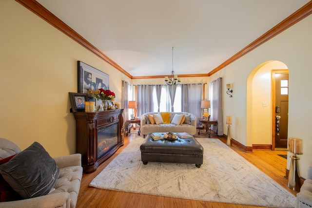 living room featuring arched walkways, crown molding, a chandelier, wood finished floors, and baseboards