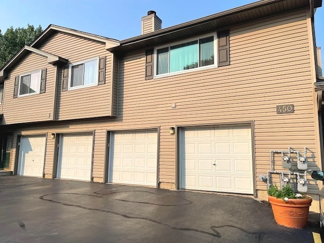 exterior space with a garage, a chimney, and asphalt driveway