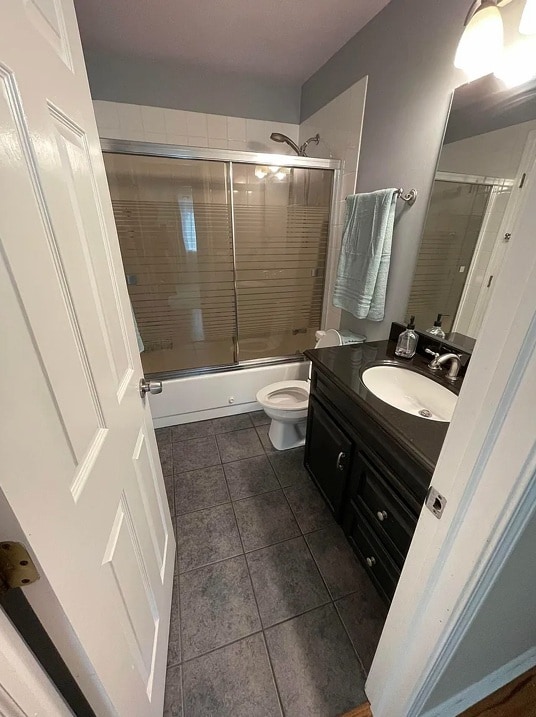 full bath featuring tile patterned flooring, vanity, shower / bath combination with glass door, and toilet