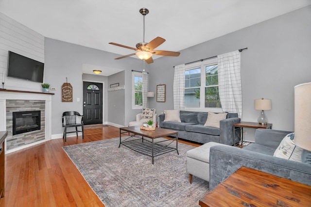 living area with wood finished floors, ceiling fan, a tiled fireplace, and baseboards
