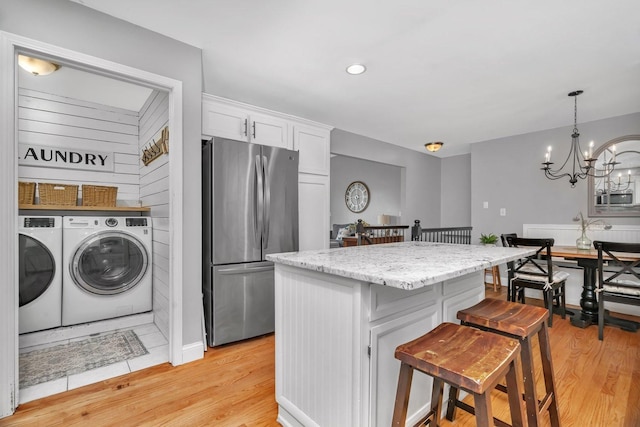 kitchen featuring freestanding refrigerator, washing machine and clothes dryer, white cabinetry, a kitchen bar, and a kitchen island