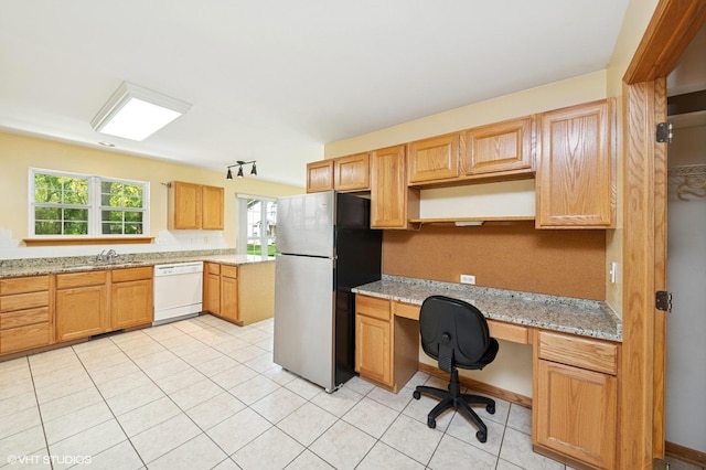 kitchen with freestanding refrigerator, white dishwasher, a sink, light stone countertops, and light tile patterned floors