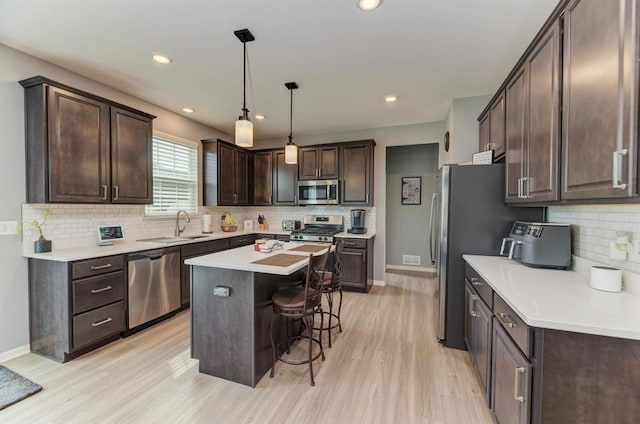 kitchen featuring stainless steel appliances, a sink, dark brown cabinets, a breakfast bar, and tasteful backsplash
