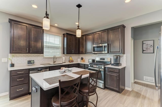kitchen featuring appliances with stainless steel finishes, a sink, dark brown cabinetry, light wood finished floors, and decorative backsplash