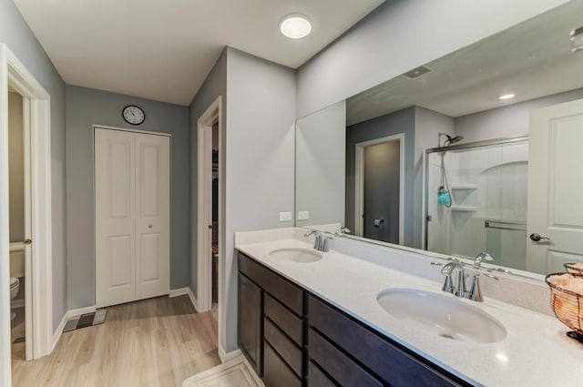 bathroom featuring wood finished floors, a shower stall, toilet, double vanity, and baseboards