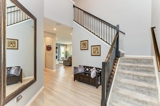 stairs with wood finished floors, recessed lighting, baseboards, and a high ceiling