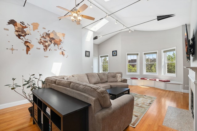 living room featuring track lighting, light wood-style floors, ceiling fan, a skylight, and high vaulted ceiling