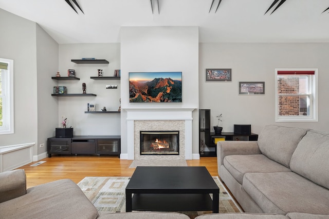 living area with light wood-style flooring, a glass covered fireplace, and baseboards