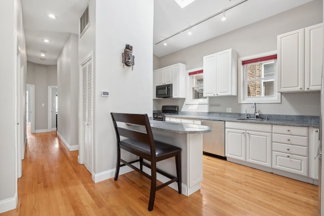 kitchen with stainless steel appliances, a sink, rail lighting, a kitchen breakfast bar, and white cabinetry