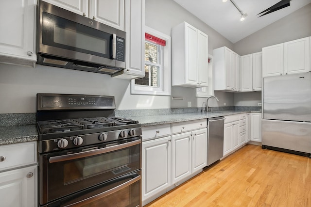 kitchen featuring appliances with stainless steel finishes, a sink, vaulted ceiling, white cabinets, and light wood-style floors