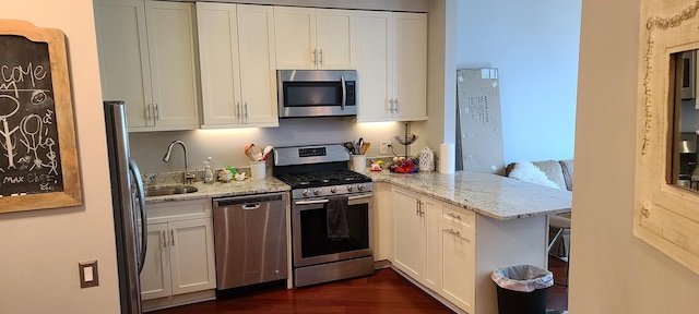 kitchen with stainless steel appliances, a sink, a peninsula, white cabinetry, and light stone countertops