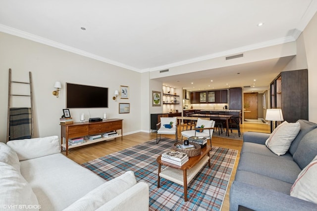 living room featuring light wood finished floors, ornamental molding, baseboards, and recessed lighting