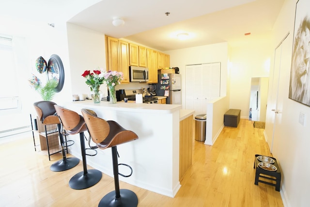 kitchen featuring stainless steel appliances, light brown cabinets, light wood finished floors, a breakfast bar, and light countertops