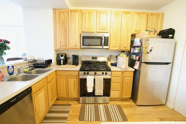 kitchen with appliances with stainless steel finishes, light brown cabinets, a sink, and light wood finished floors