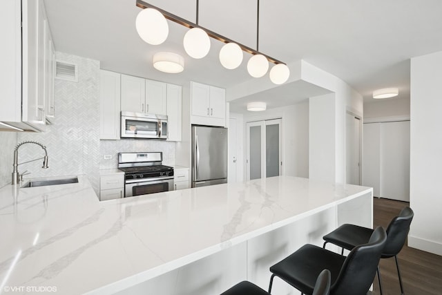 kitchen with stainless steel appliances, a sink, backsplash, dark wood-style floors, and light stone countertops