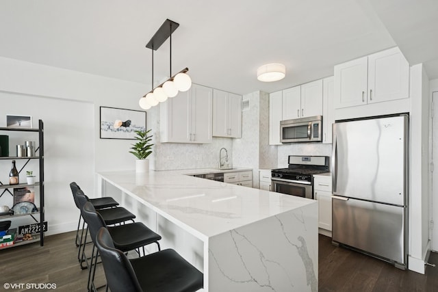 kitchen with appliances with stainless steel finishes, a sink, a peninsula, decorative backsplash, and white cabinets