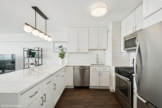 kitchen featuring appliances with stainless steel finishes, a sink, a peninsula, dark wood-type flooring, and white cabinets