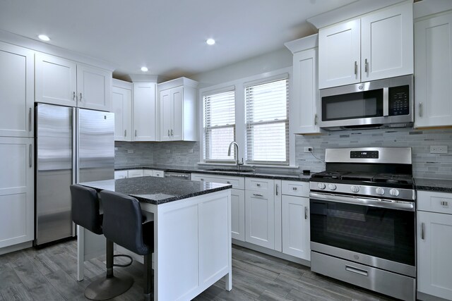 6211 W School St, Chicago, IL 60634 - kitchen featuring stainless steel appliances, a sink, white cabinets, dark stone countertops, and a center island