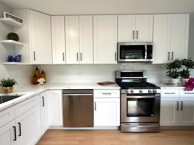 kitchen featuring appliances with stainless steel finishes, open shelves, light wood-style flooring, and white cabinetry