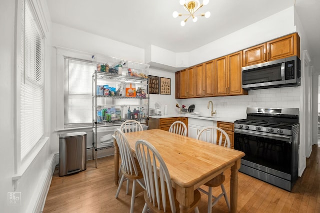kitchen featuring appliances with stainless steel finishes, a sink, light wood finished floors, brown cabinetry, and tasteful backsplash
