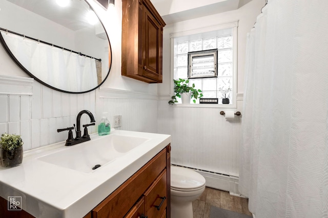 full bath featuring toilet, vanity, baseboard heating, and wainscoting